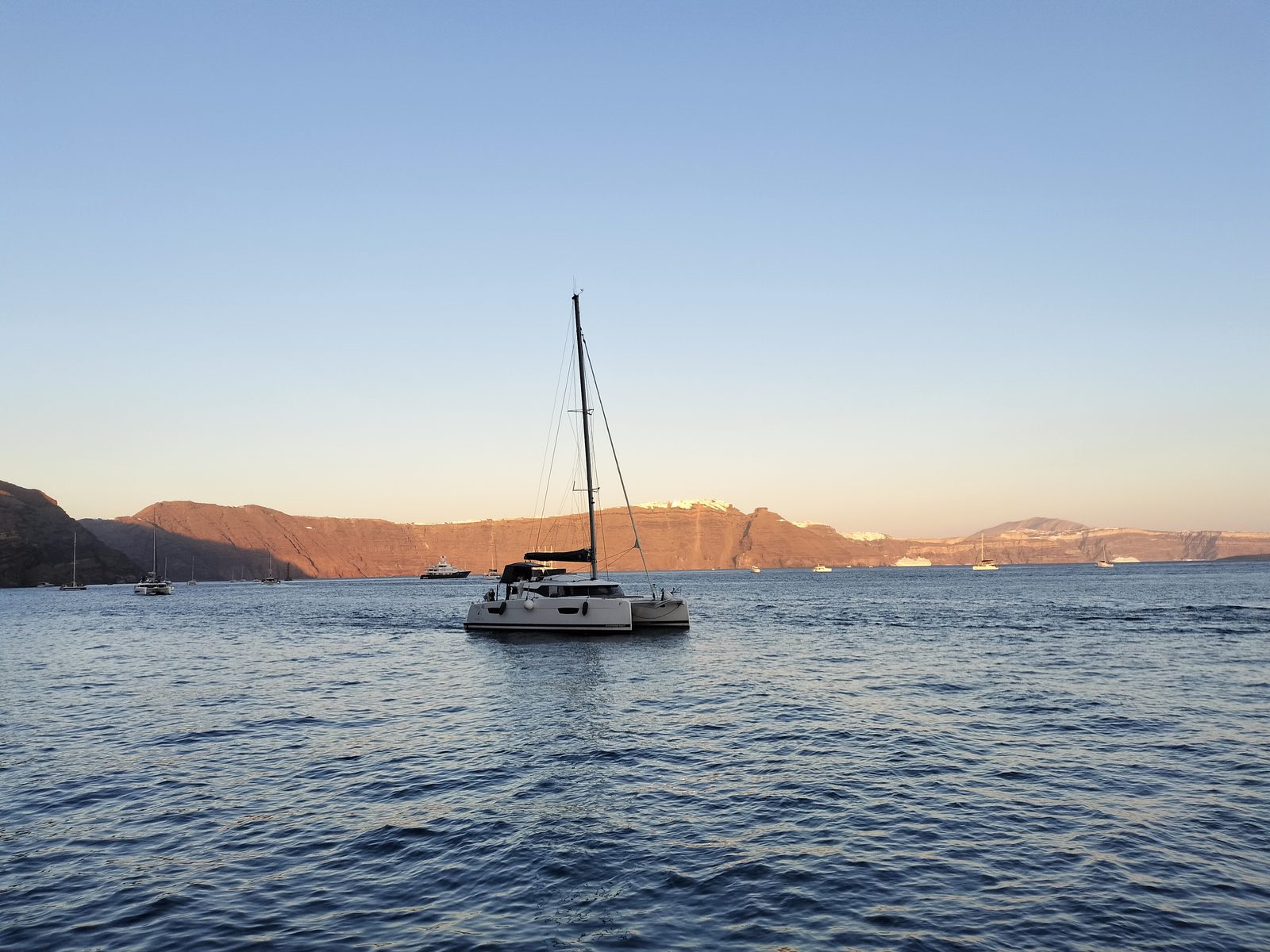 夕暮れのカルデラを行くクルーズ船 Catamaran sailing the caldera at sunset, Santorini